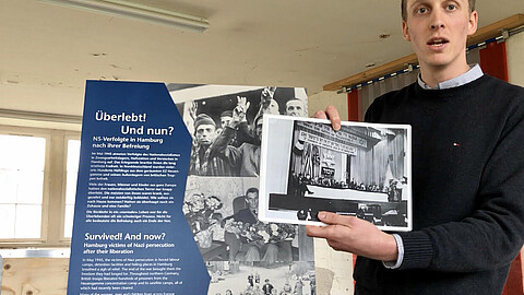 Foto von Lennart Onken im Depot der KZ-Gedenkstätte Neuengamme vor einer Ausstellungstafel